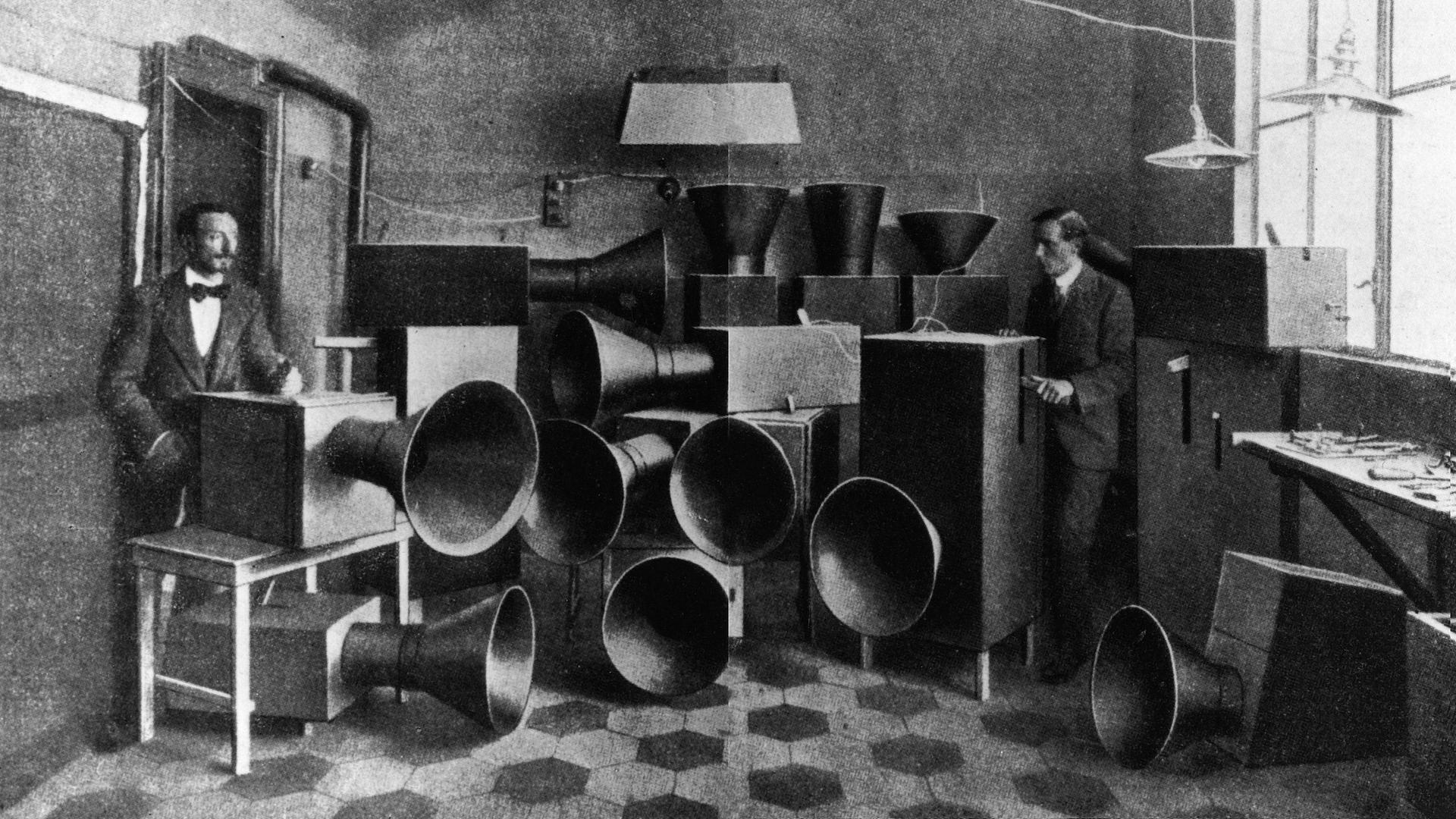 Luigi Russolo und sein Assistent Ugo Piatti im Jahr 1914 neben Kisten mit großen Schalltrichtern, den legendären Geräuschinstrumenten