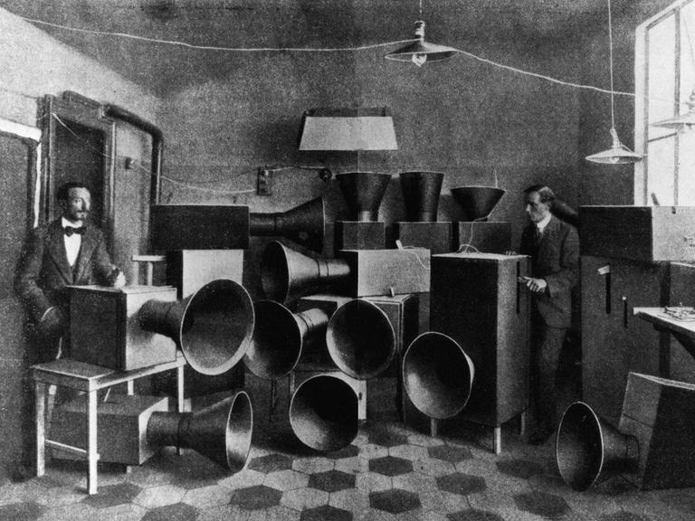 Luigi Russolo und sein Assistent Ugo Piatti im Jahr 1914 neben Kisten mit großen Schalltrichtern, den legendären Geräuschinstrumenten