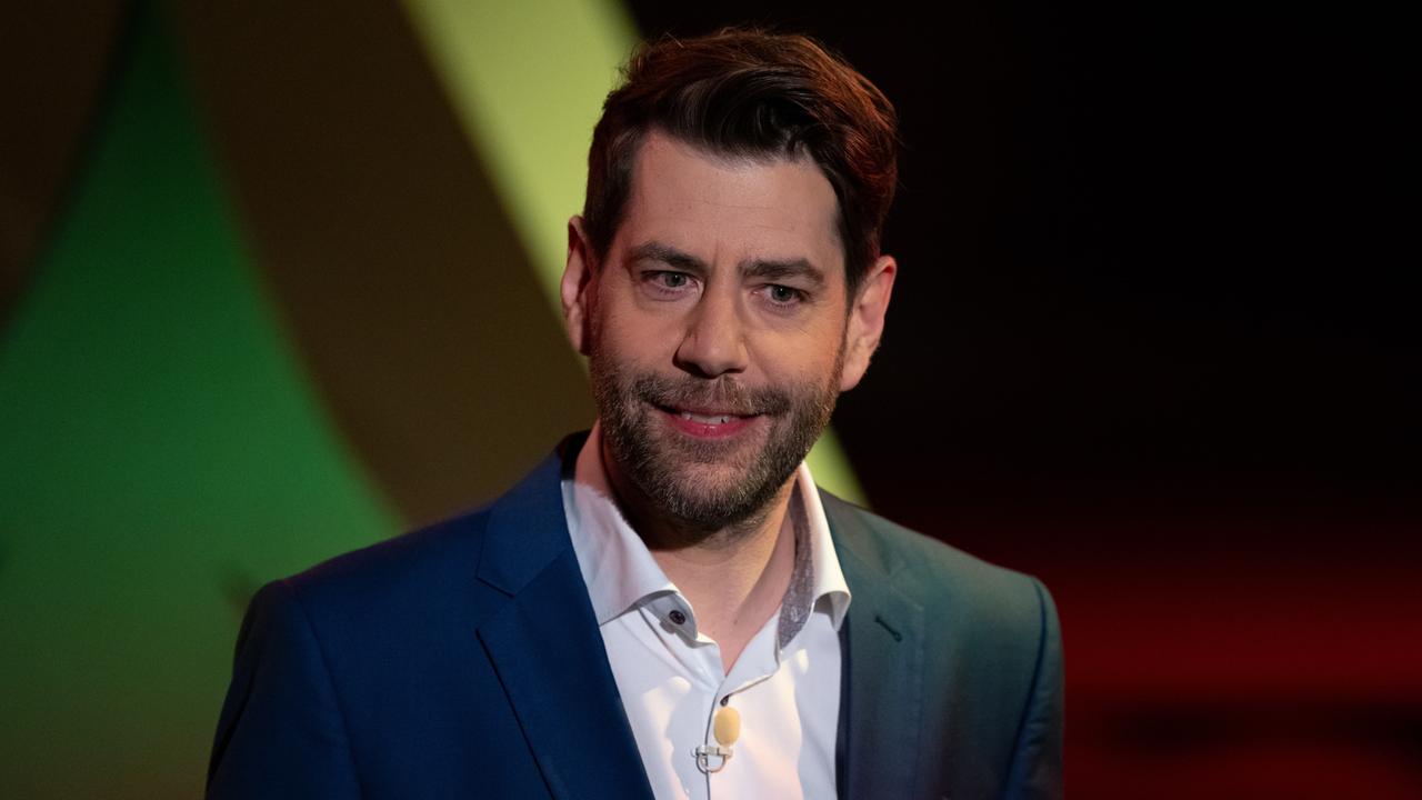 Claus von Wagner steht lächelnd vor einem grünen Hintergrund