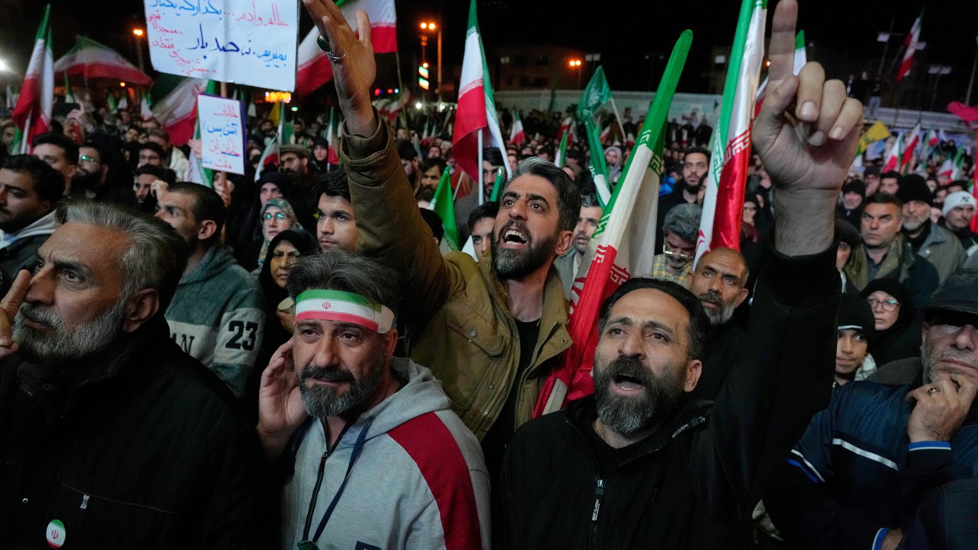 Viele Menschen stehen nebeneinander und schwenken Fahnen in rot, weiß und grün. Sie heben die Arme und rufen etwas.