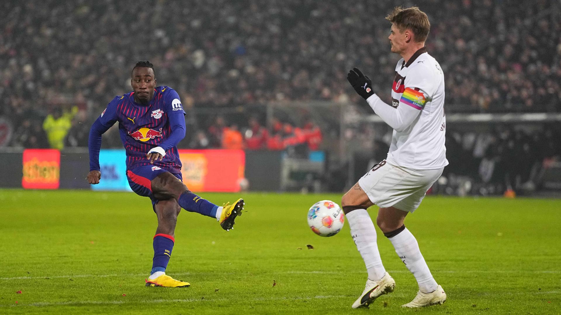 Ein Fußballspieler von RB Leipzig schießt den Ball, ein Gegenspieler versucht abzuwehren.