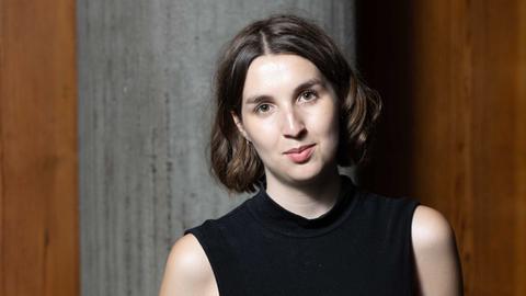 Portrait einer jungen Frau, die an eine Wand gelehnt lächelnd in die Kamera blickt