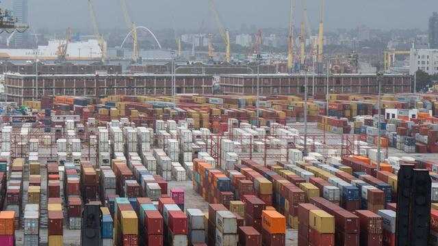 Blick auf viele farbige Container im Hafen von Montevideo in Uruguay. Dahinter verschwommener Kräne und Häuser der Stadt.