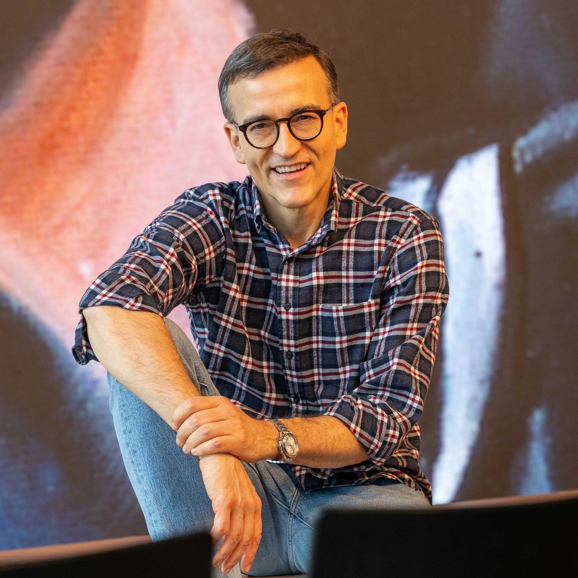 Daniel Schreiber sitzt vor einer Stuhlreihe und schaut lächelnd in die Kamera