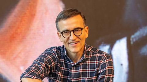 Daniel Schreiber sitzt vor einer Stuhlreihe und schaut lächelnd in die Kamera