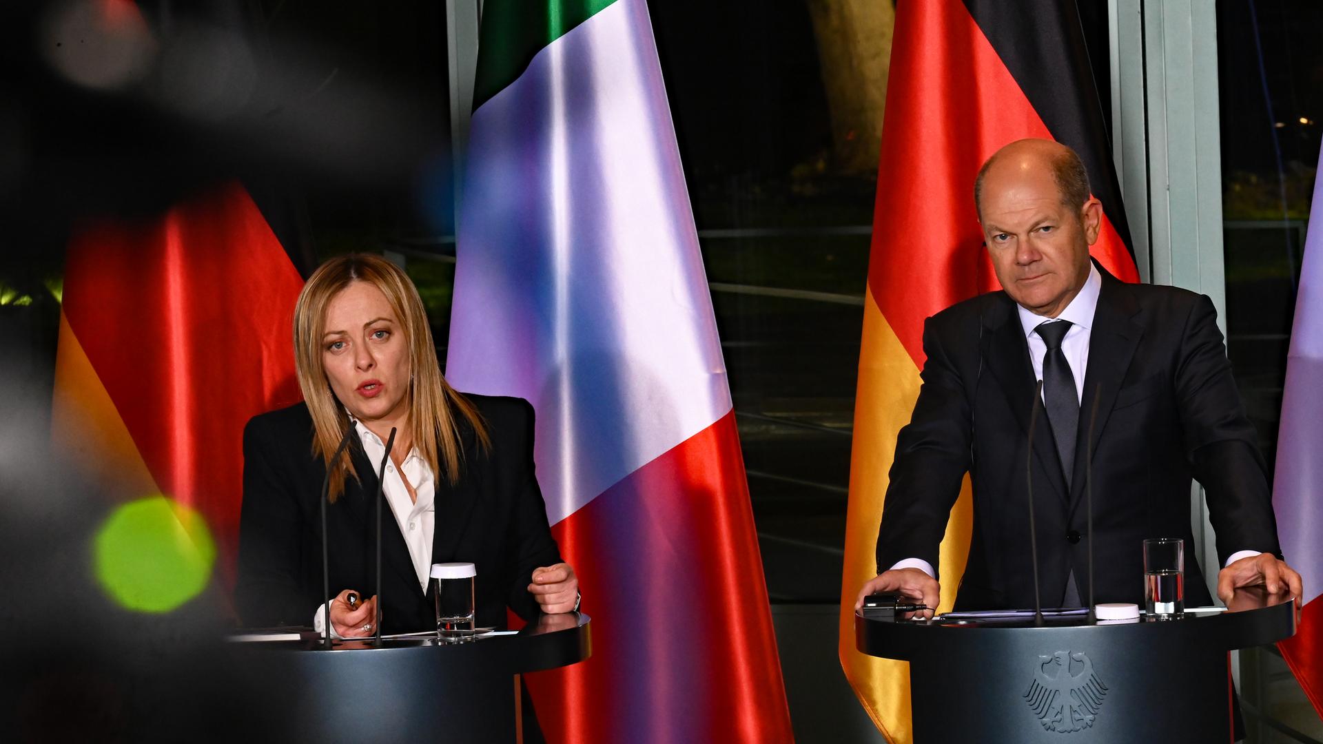 Bundeskanzler Olaf Scholz und Giorgia Meloni, Ministerpräsidentin von Italien, stehen bei einer gemeinsamen Pressekonferenz nebeneinander an Stehpulten mit Mikrofonen. Im Hintergrund sind die Flaggen beider Länder zu sehen.