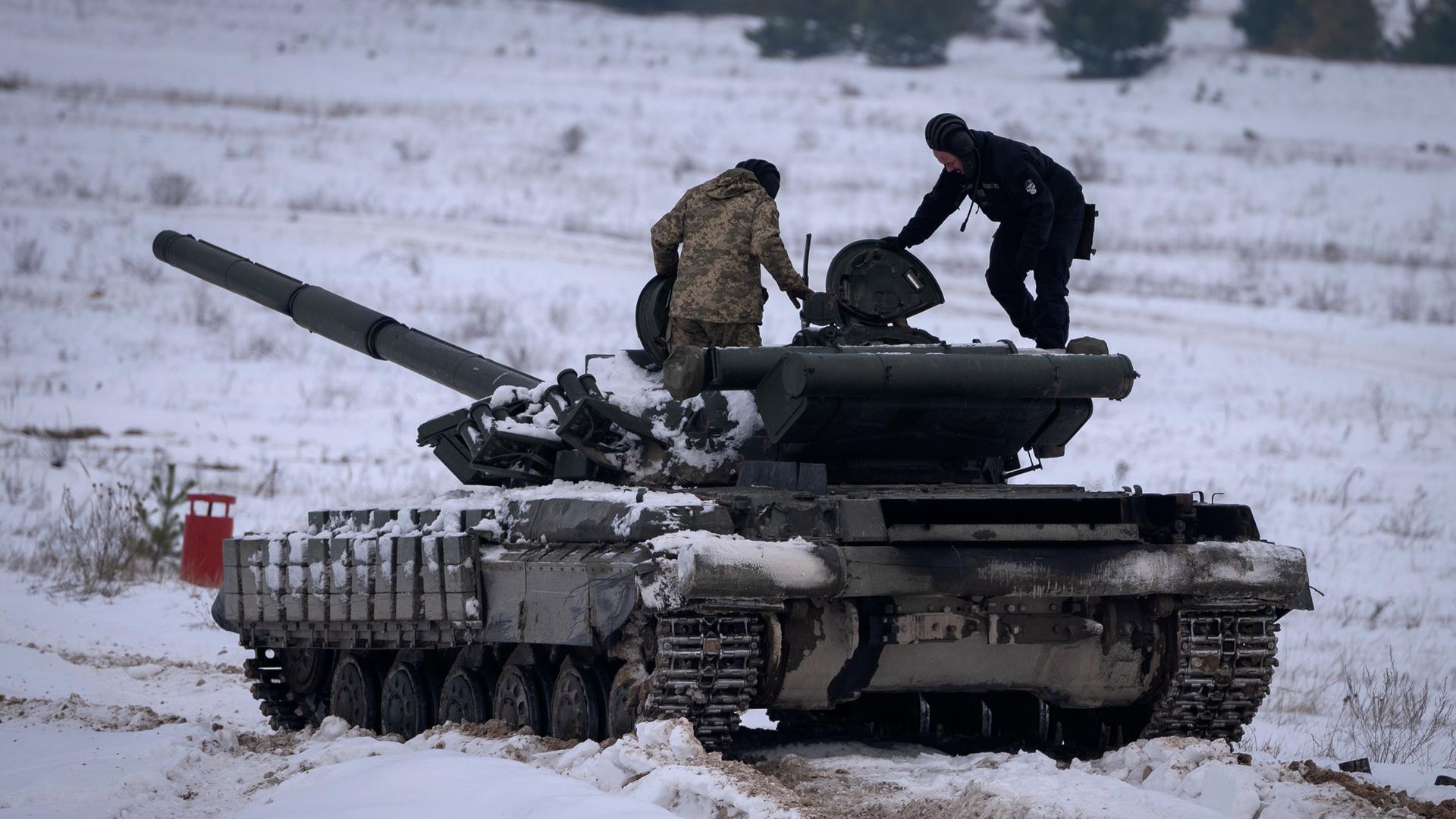 Zwei Personen steigen aus einem Panzer. Der Panzer steht im Schnee.