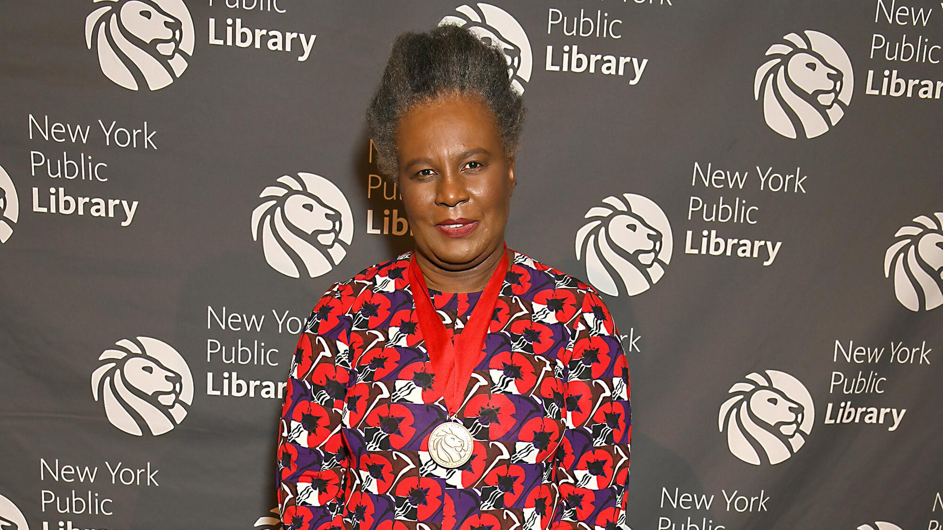Claudia Rankine lächelt in die Kamera. Sie trägt ein langes Kleid mit rot-blauem Blumenmuster. Claudia Rankine lächelt in die Kamera. Sie trägt ein langes Kleid mit rot-blauem Blumenmuster.