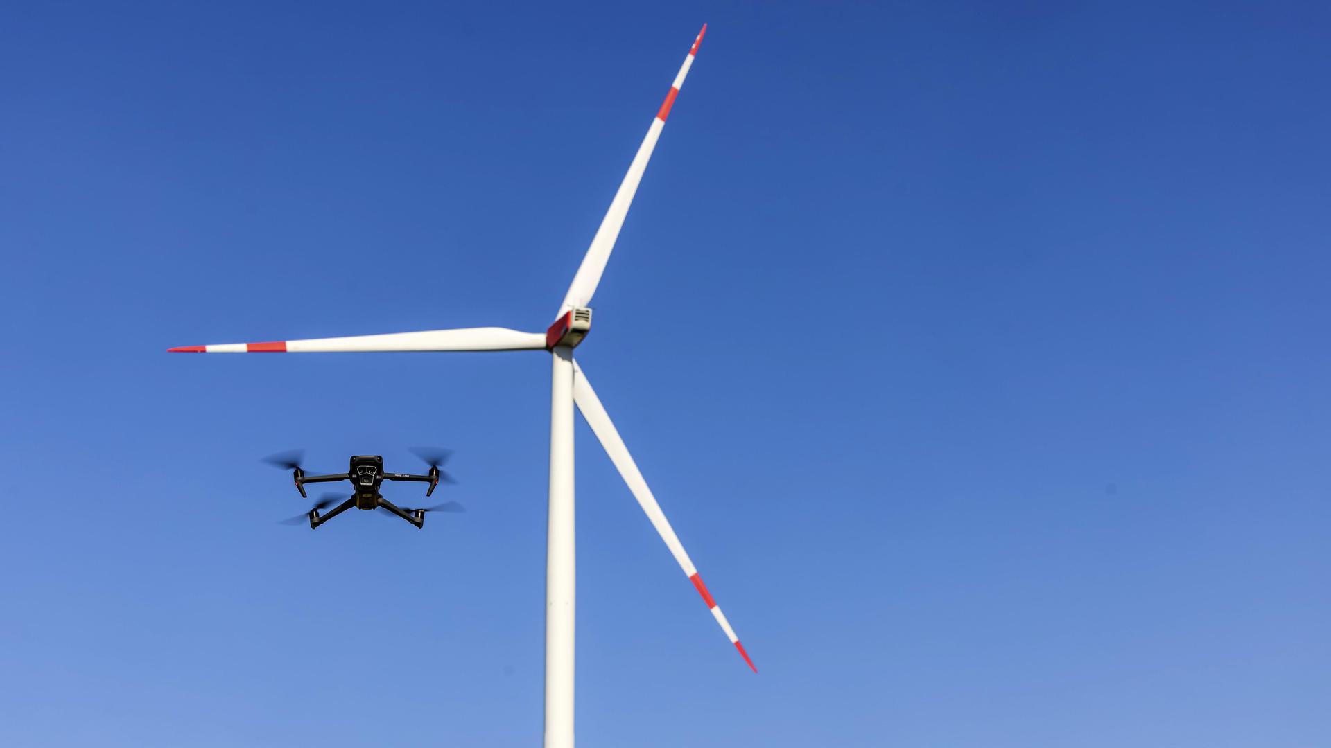 Eine Drohne fliegt vor einem Windrad in einem Windpark.