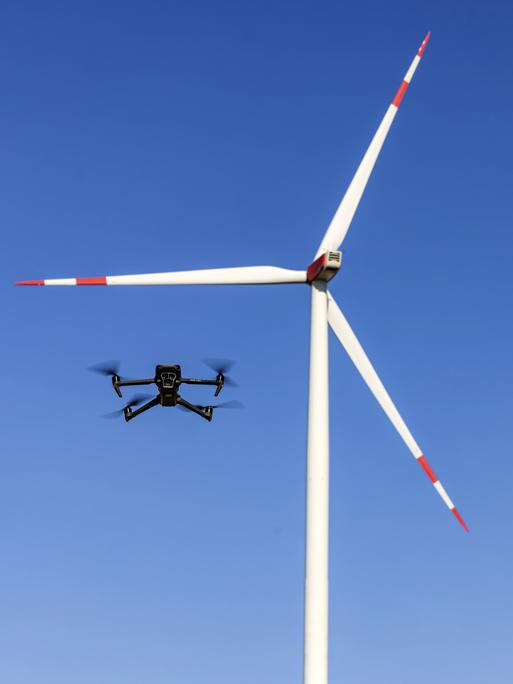Eine Drohne fliegt vor einem Windrad in einem Windpark.