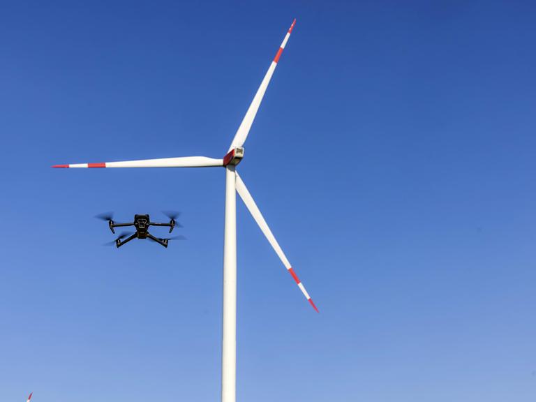 Eine Drohne fliegt vor einem Windrad in einem Windpark.