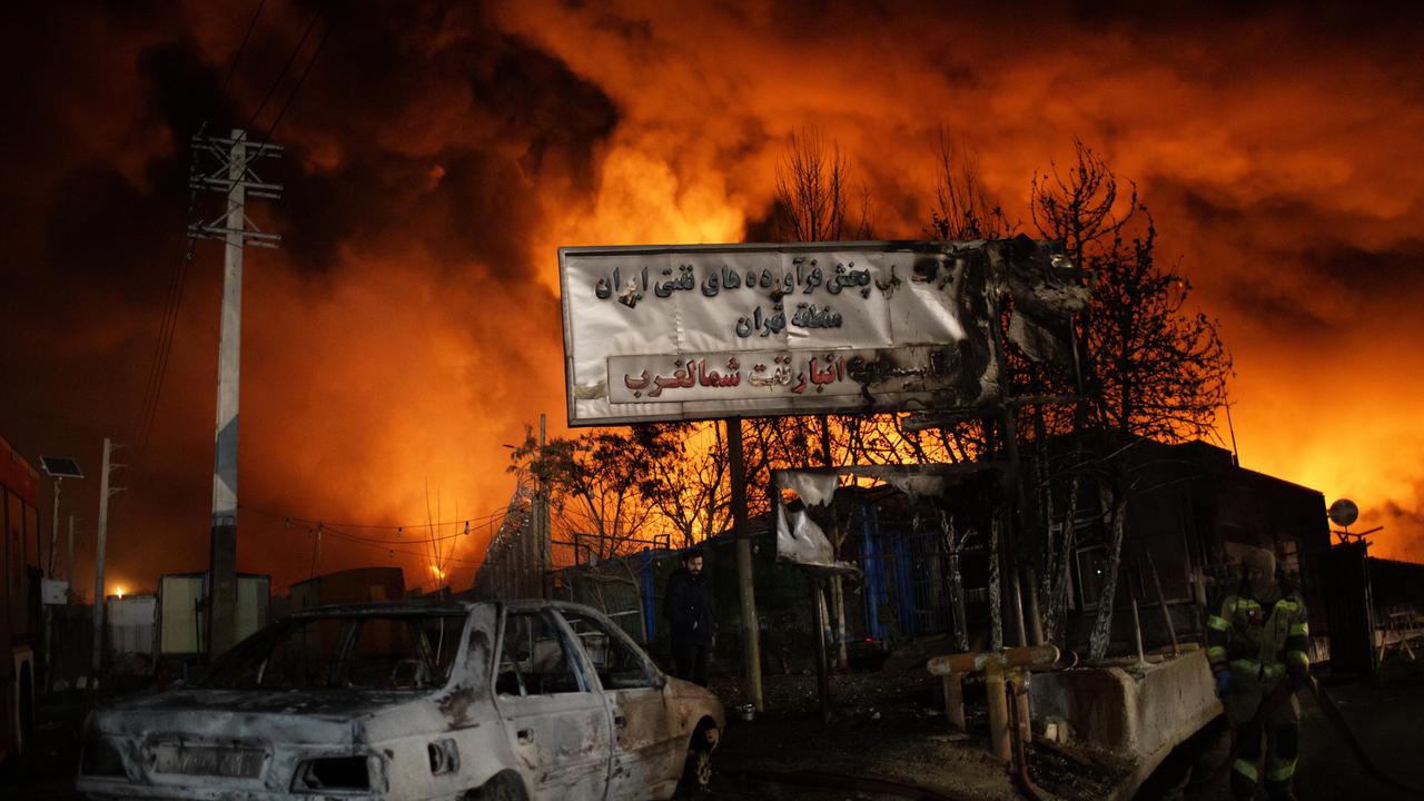 Nach Angriffen der USA und Israels bricht am 8.3.2026 im Öllager von Shahran in Iran ein Feuer aus. Zu sehen ist ein ausgebranntes Auto und ein Schild vor gelben Feuerflammen.