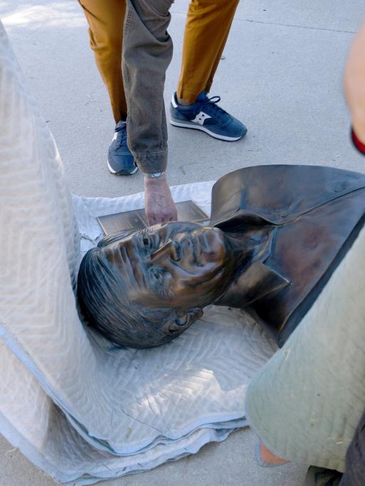 Mitarbeitende der Stadt haben eine Bronze-Büste von Cesar Chavez auf eine Decke gelegt und transportieren sie ab. 