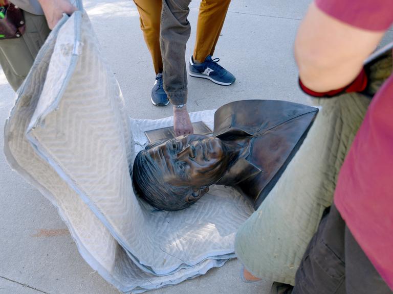 Mitarbeitende der Stadt haben eine Bronze-Büste von Cesar Chavez auf eine Decke gelegt und transportieren sie ab. 