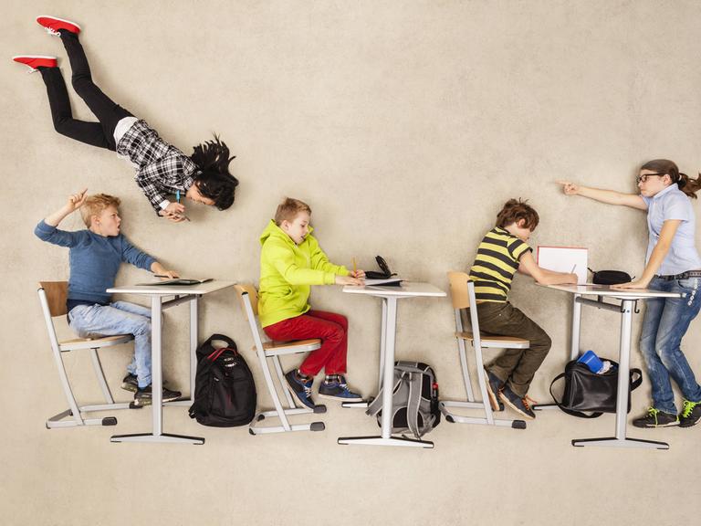 Schulkinder auf Stühlen und an Tischen schweben durch eine Klasse.