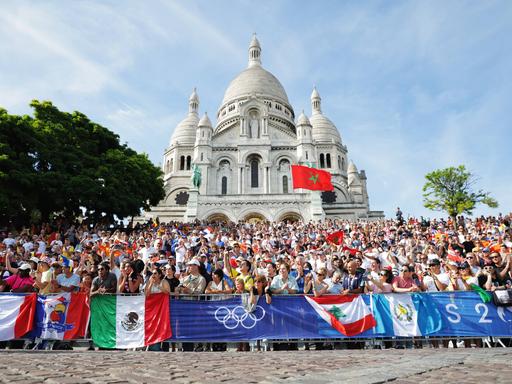 Bei den Olympischen Spielen 2024 in Paris stehen Fans an der Straßenrad-Rennstrecke, die durch Montmartre führt.