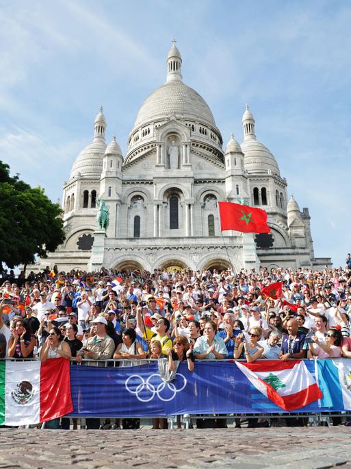 Bei den Olympischen Spielen 2024 in Paris stehen Fans an der Straßenrad-Rennstrecke, die durch Montmartre führt.