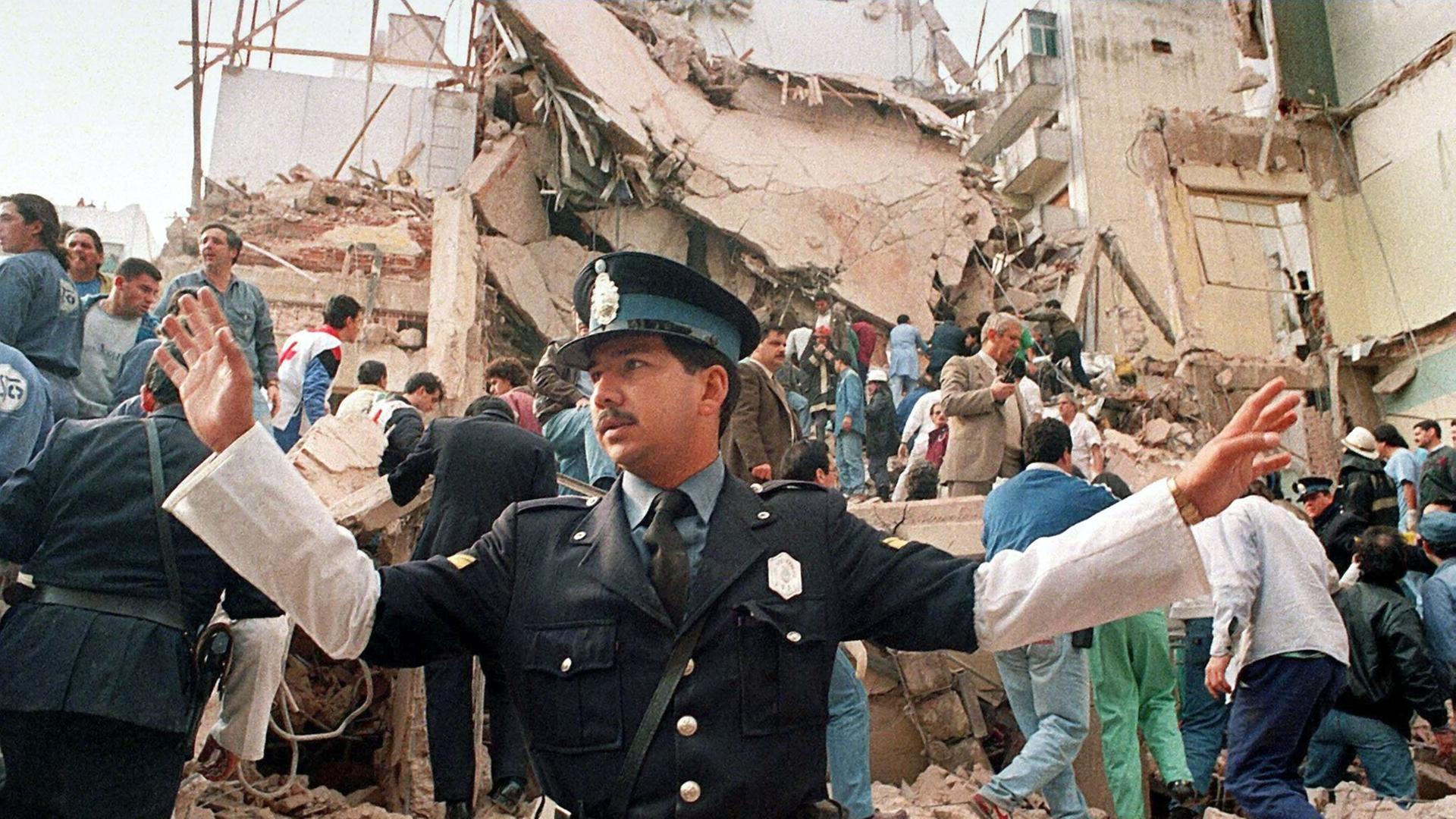 Das Foto aus dem Jahr 1994 zeigt Menschen, die im völlig zerstörten jüdischen Gemeindezentrum in Buenos Aires in Trümmern nach Überlebenden suchen. Im Vordergrund steht ein Polizist mit ausgebreiteten Armen. Das Foto aus dem Jahr 1994 zeigt Menschen, die im völlig zerstörten jüdischen Gemeindezentrum in Buenos Aires in Trümmern nach Überlebenden suchen. Im Vordergrund steht ein Polizist mit ausgebreiteten Armen.