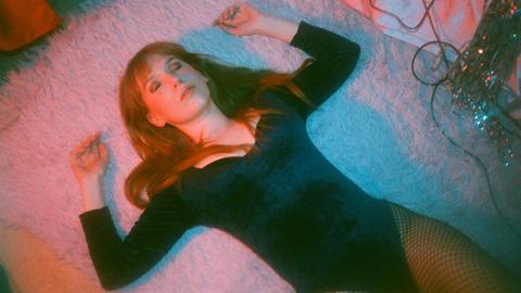 Die Schaupielerin und Musikerin Christin Nichols liegt mit geschlossenen Augen auf einem Teppichboden.