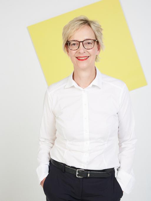 Christine Regitz hat kurzes, blondes Haar. Sie trägt eine weiße Bluse und eine braune Hornbrille.