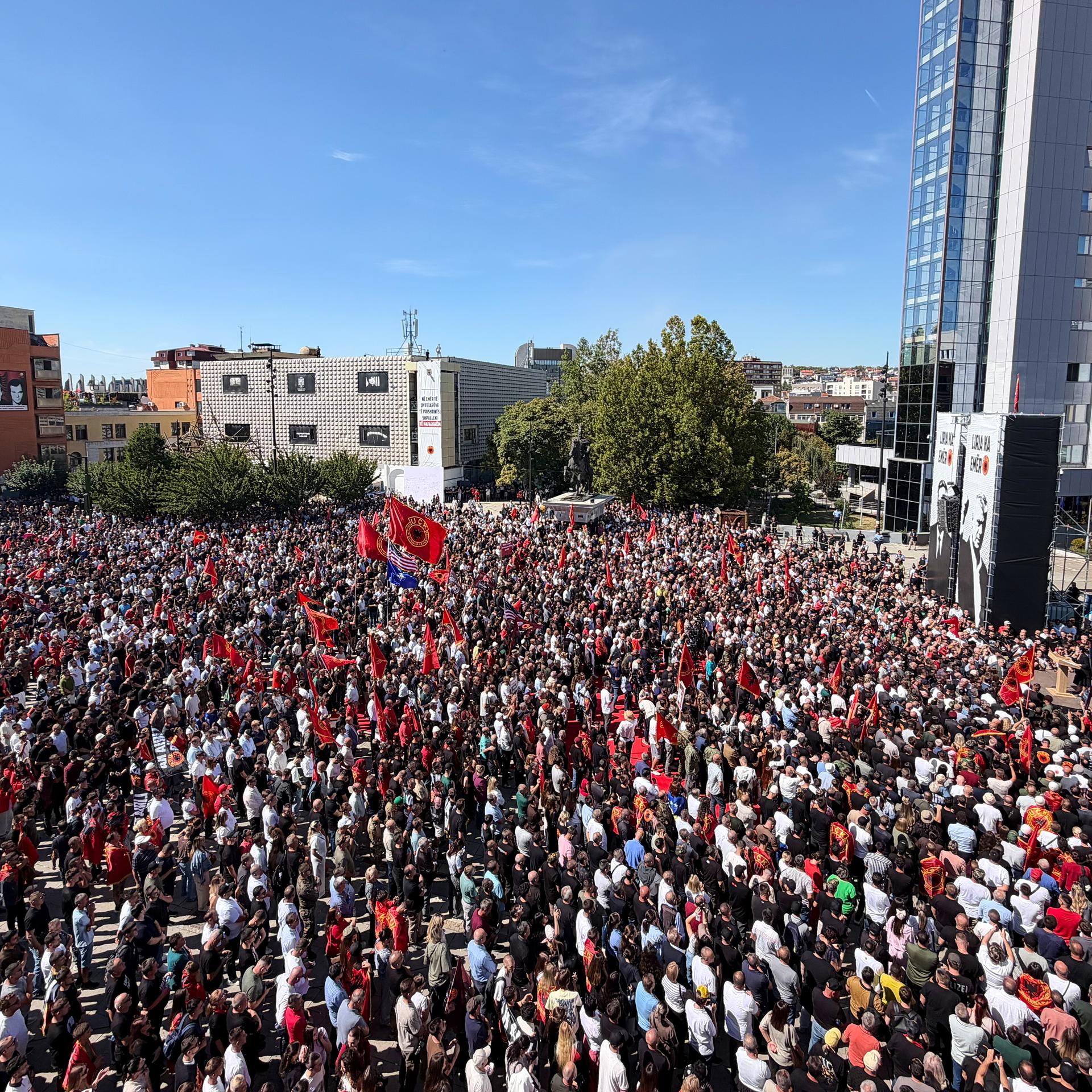 Tausende Menschen versammeln sich auf einem Platz, manche schwenken rote Fahnen.