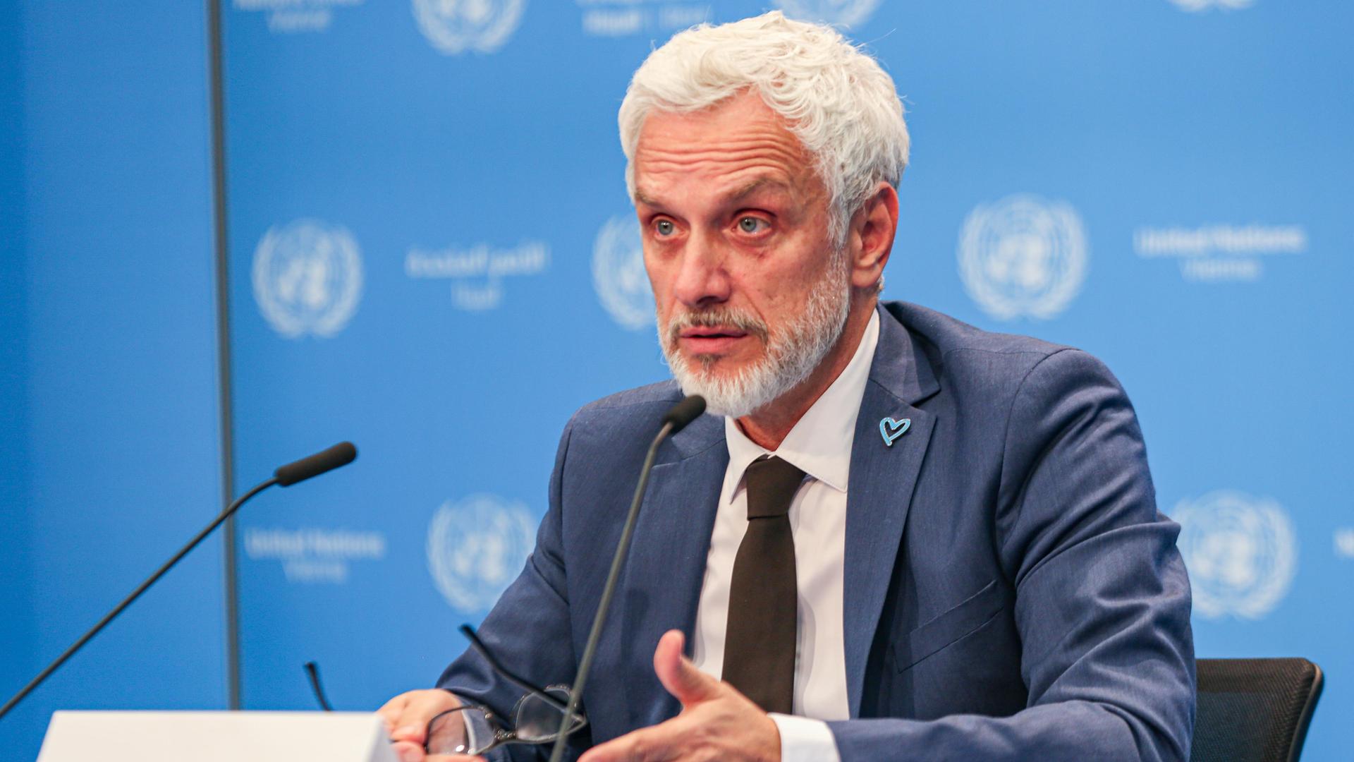 Ilias Chatzis, Leiter der Sektion Menschenhandel und Menschenschmuggel des UNODC, spricht in ein Mikrofon, im Hintergrund eine blaue Wand und das Logo der Vereinten Nationen.