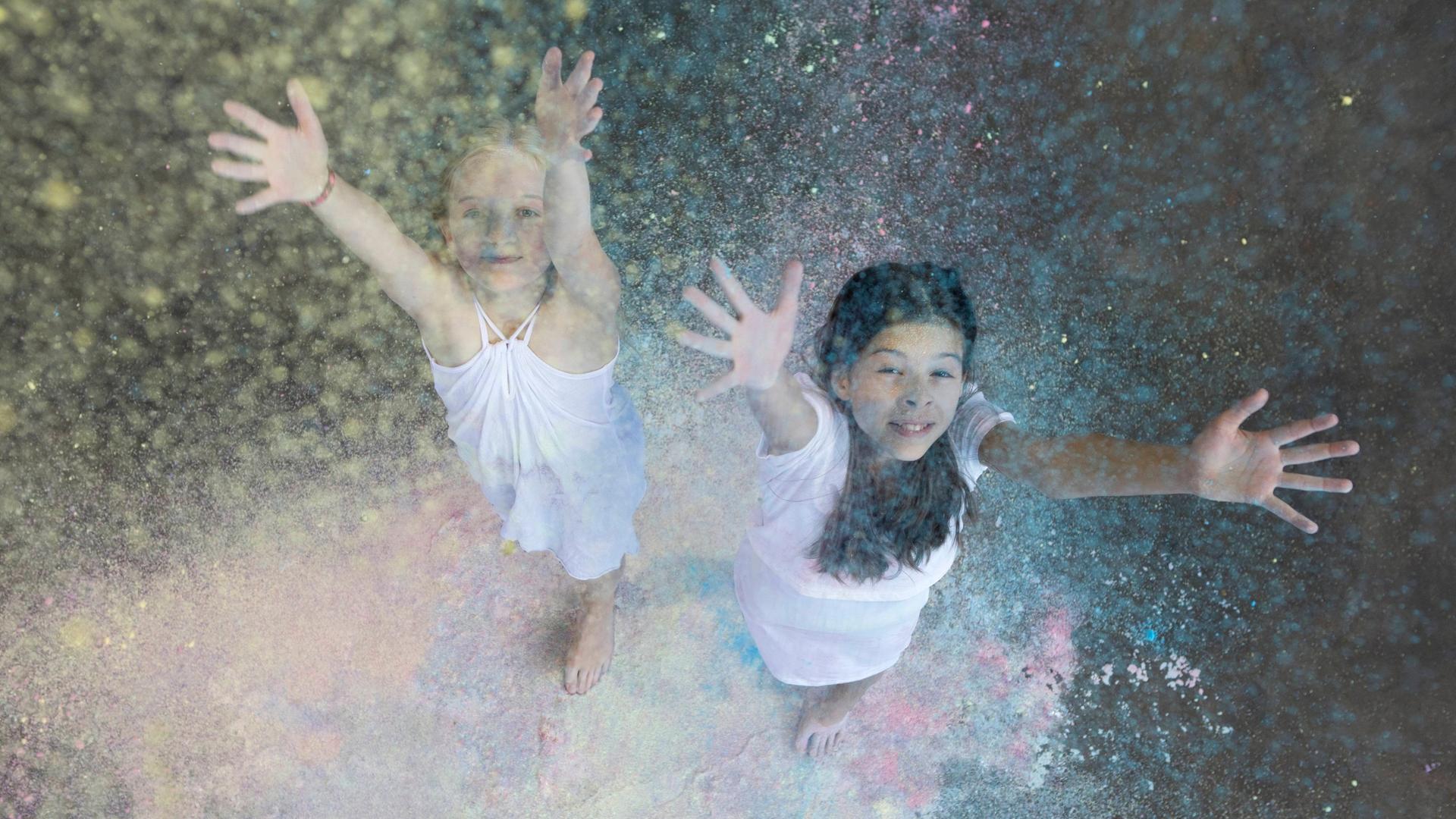 Zwei Mädchen werfen Farbpulver in die Luft. 