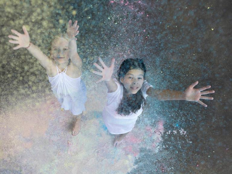 Zwei Mädchen werfen Farbpulver in die Luft. 