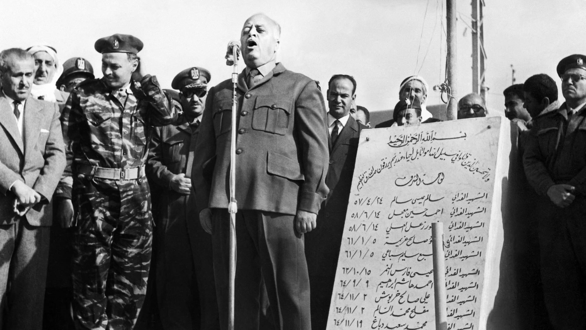 Historisches Schwarzweißfoto von Ahmed Shukeiri, der auf einer Bühne in ein Mikrofon spricht.