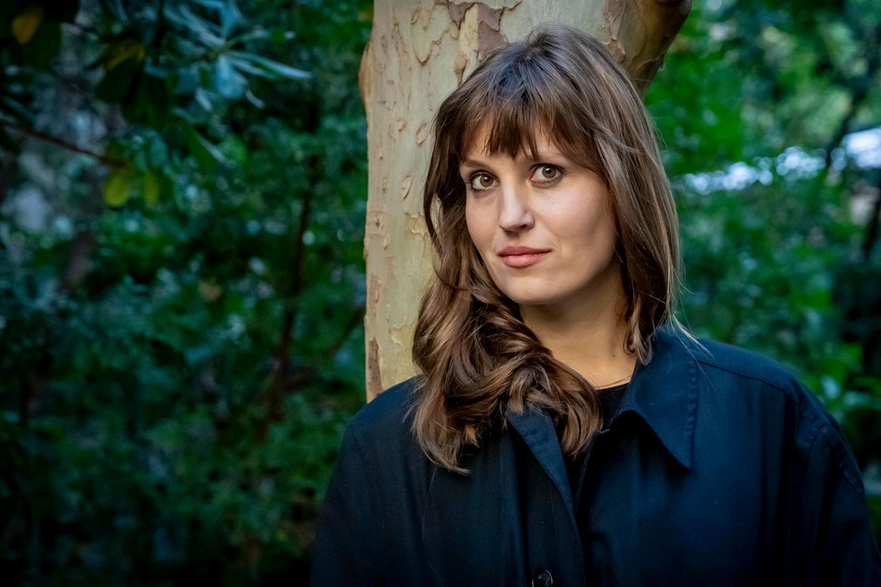 Eine Frau lehnt an einem Baum und schaut in die Kamera: die Schriftstellerin Charlotte Gneuß.