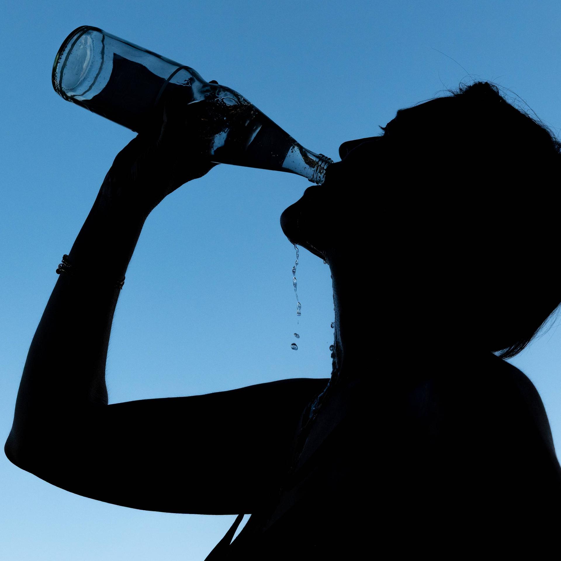 Die Silhouette einer Frau, die aus einer Mineralwasserflasche trinkt, ist vor blauem Hintergrund zu sehen.