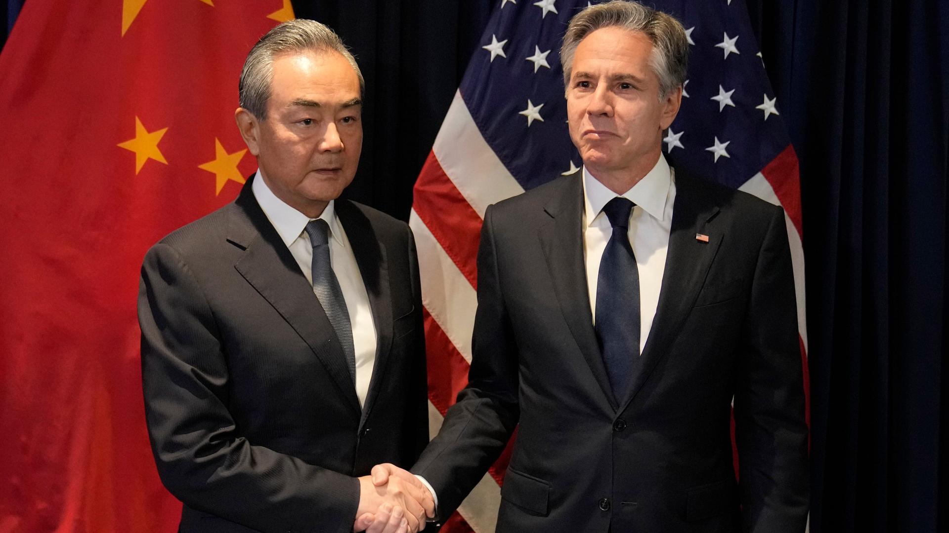 Zwei Männer in dunklen Anzügen und mit grauen Haaren schütteln Hände, sie schauen ernst, im Hintergund sind die Fahnen von China und den USA zu sehen. 13.07.2023. Zwei Männer in dunklen Anzügen und mit grauen Haaren schütteln Hände, sie schauen ernst, im Hintergund sind die Fahnen von China und den USA zu sehen. 13.07.2023.