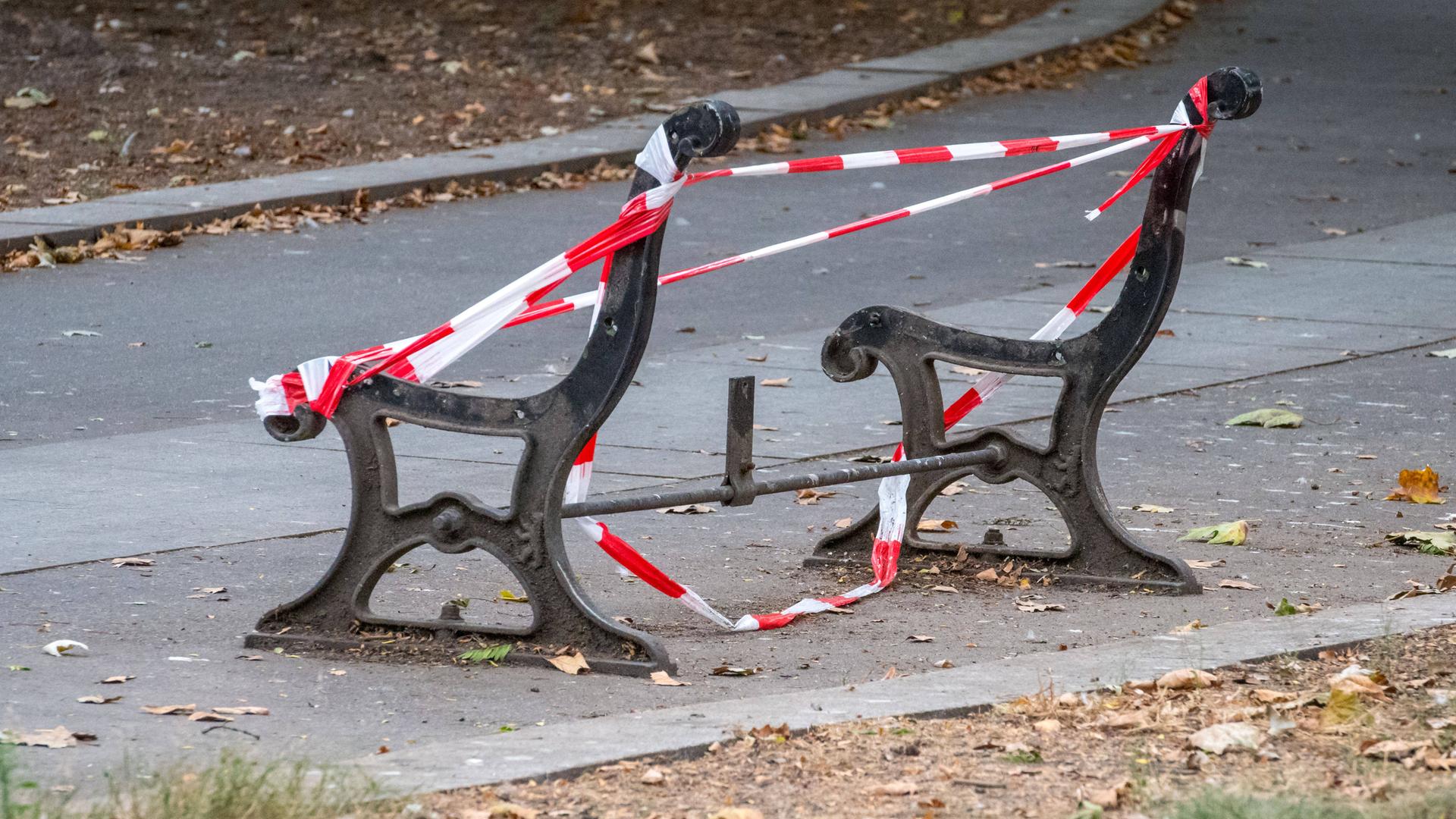 Grundgestell einer Parkbank mit Absperrband zu sehen. Der Bank fehlen Sitzfläche und Lehne.
