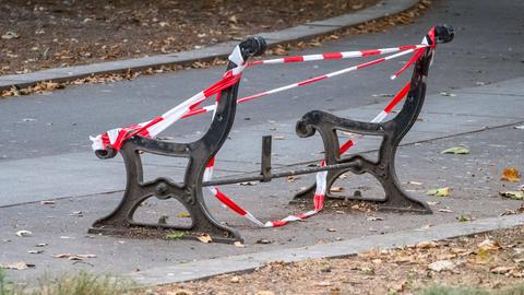 Grundgestell einer Parkbank mit Absperrband zu sehen. Der Bank fehlen Sitzfläche und Lehne.