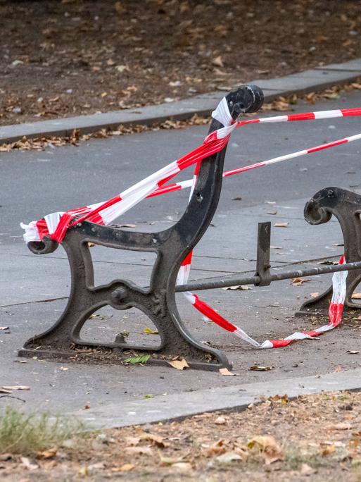 Grundgestell einer Parkbank mit Absperrband zu sehen. Der Bank fehlen Sitzfläche und Lehne.