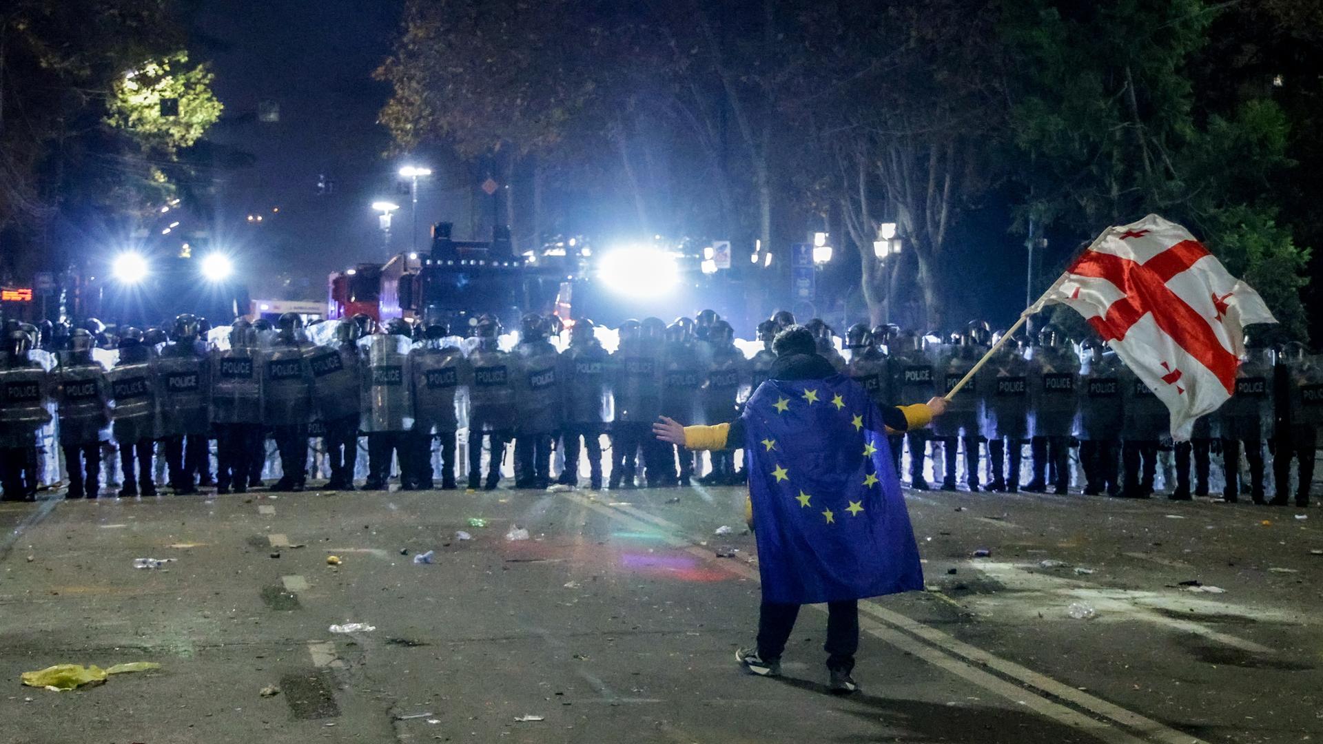 Ein Demonstrant mit EU- und Georgien-Flagge steht in Tiflis vor dem Parlamentsgebäude der Polizei gegenüber.
