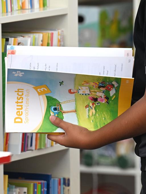 Ein Schulkind steht vor einem Regal und hält ein Arbeitsheft "Deutsch" in der Hand. Symbolbild