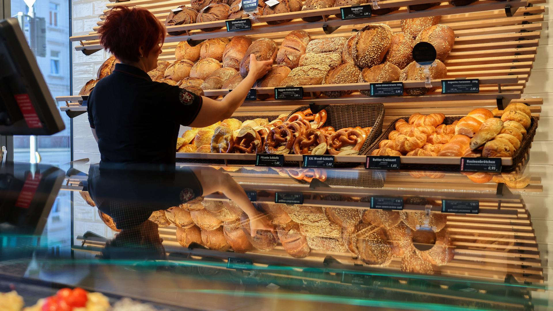 Eine Mitarbeiterin räumt Mischbrot in die Auslage einer Bäckerei.