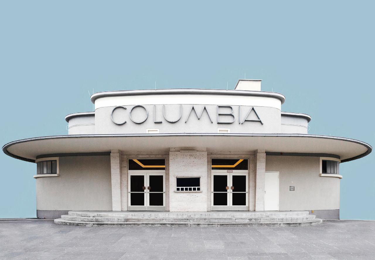 Die Fotografie der Künstlerin Sarah Eick zeigt die Columbiahalle in Berlin Tempelhof als Einzelgebäude vor einem blassblauen Hintergrund.