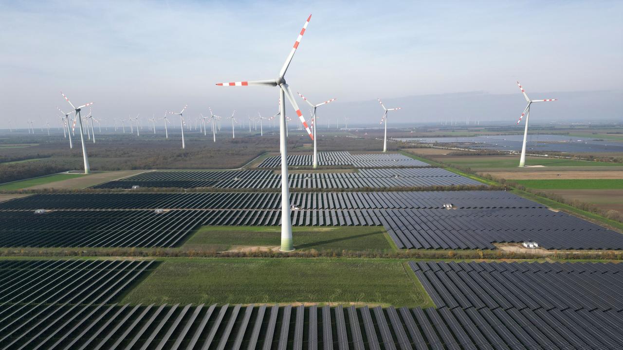 In einem Wind- und Solarpark stehen aufgereiht Windräder und große Flächen mit Solarpanels.