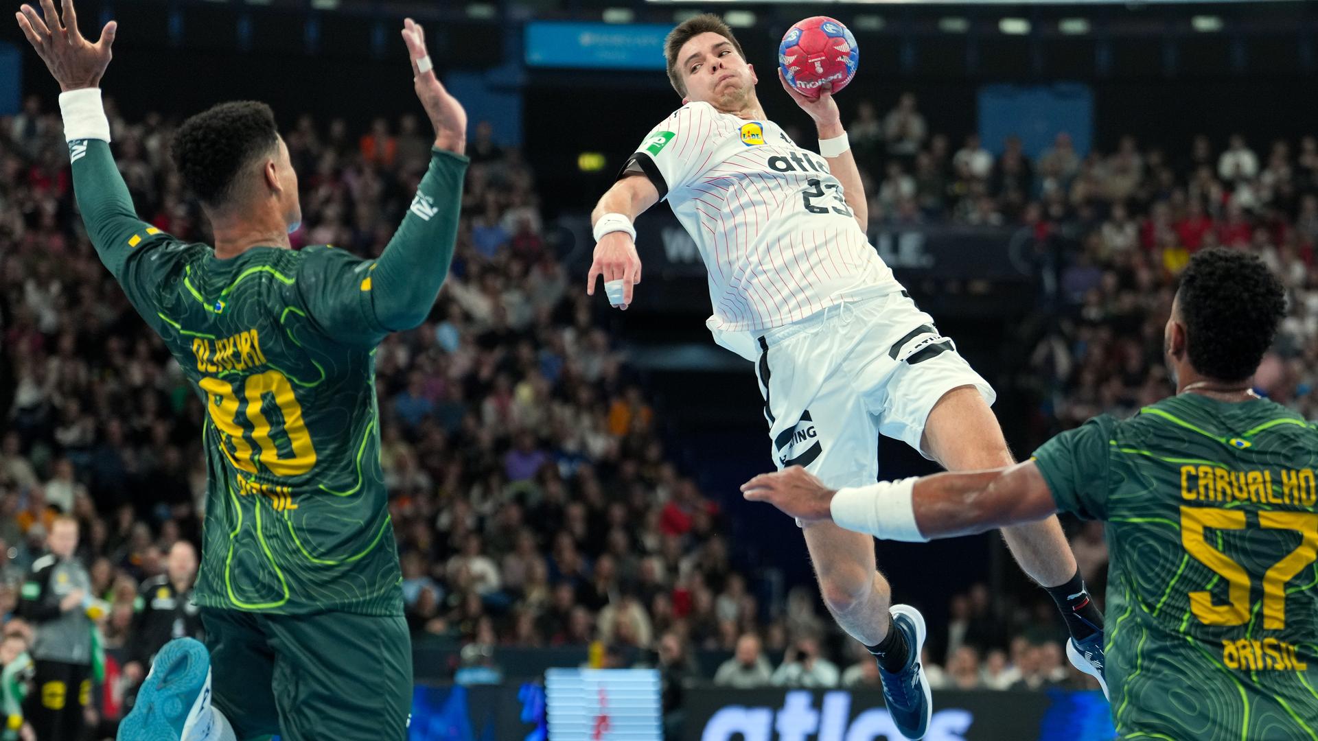 Der deutsche Handballer Renars Uscinc springt vor mehreren Abwehrspielern mit dem Ball in der Hand in die Höhe, um zum Abschluss auf das gegnerische Tor zu kommen.