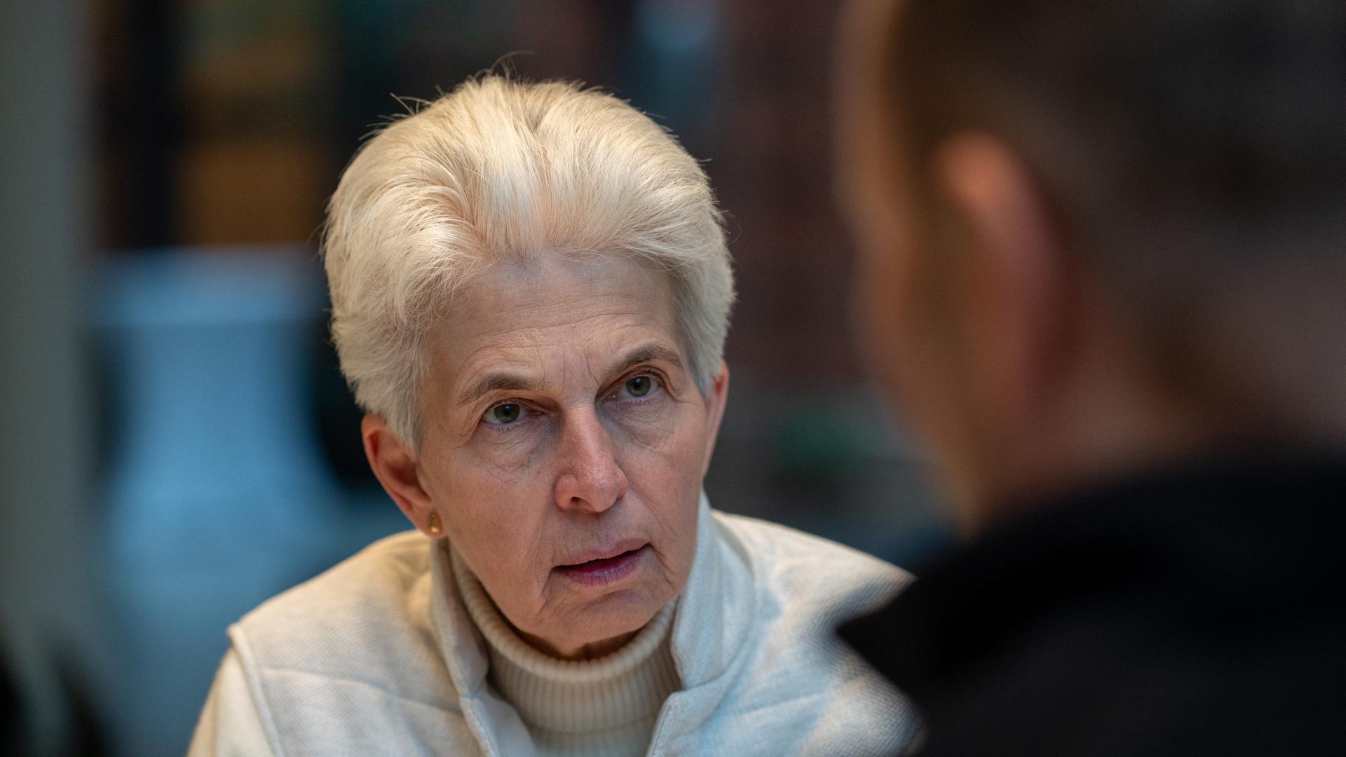 Die Verteidigungspolitikerin Marie-Agnes Strack-Zimmermann in weißem Rollkragenpullover und hellgrauer Weste. Unscharf im Vordergrund ist an der rechten Seite der Hinterkopf einer männlichen Person zu sehen, mit der sie spricht. 