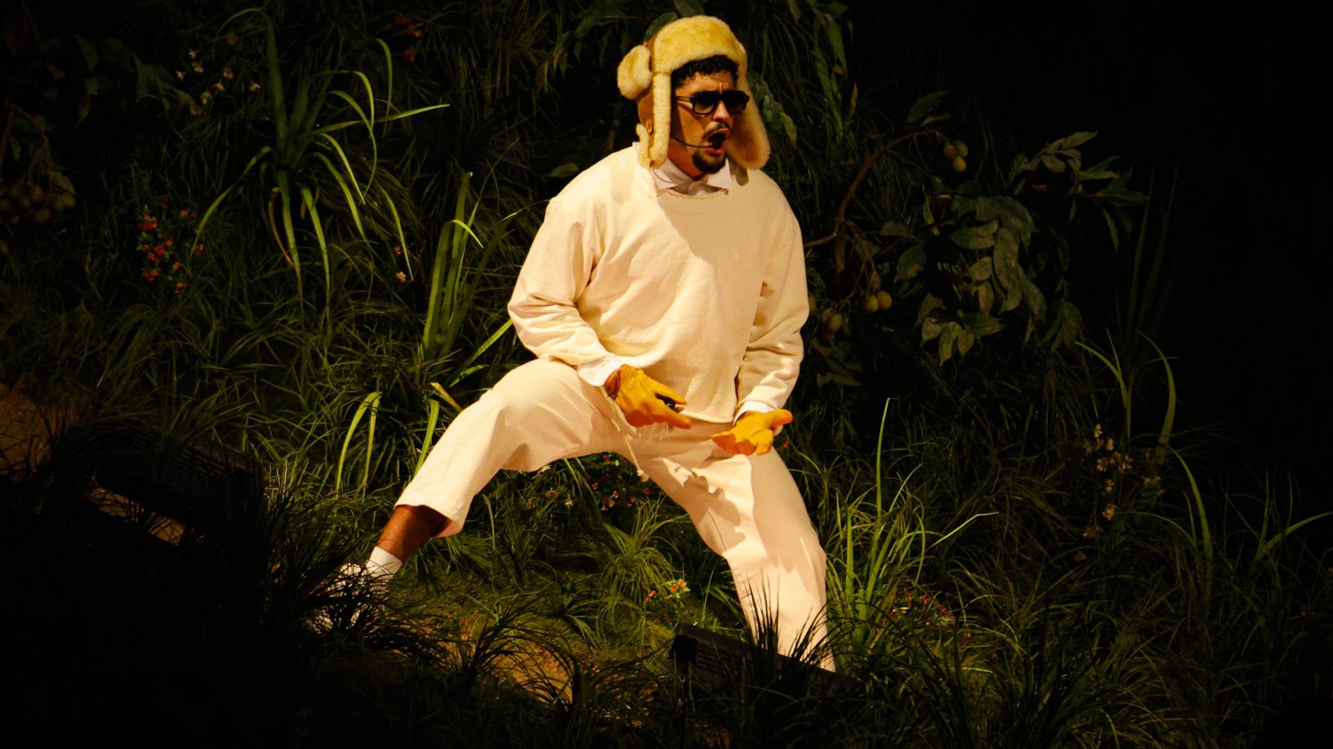 Bad Bunny steht mit einer Wintermütze auf einer Bühne und trägt Sonnenbrille, während er in ein Mikro singt