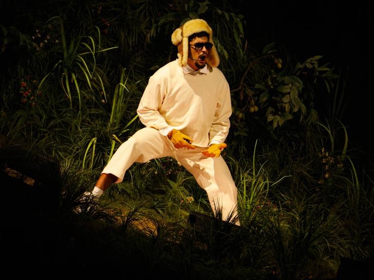 Bad Bunny steht mit einer Wintermütze auf einer Bühne und trägt Sonnenbrille, während er in ein Mikro singt