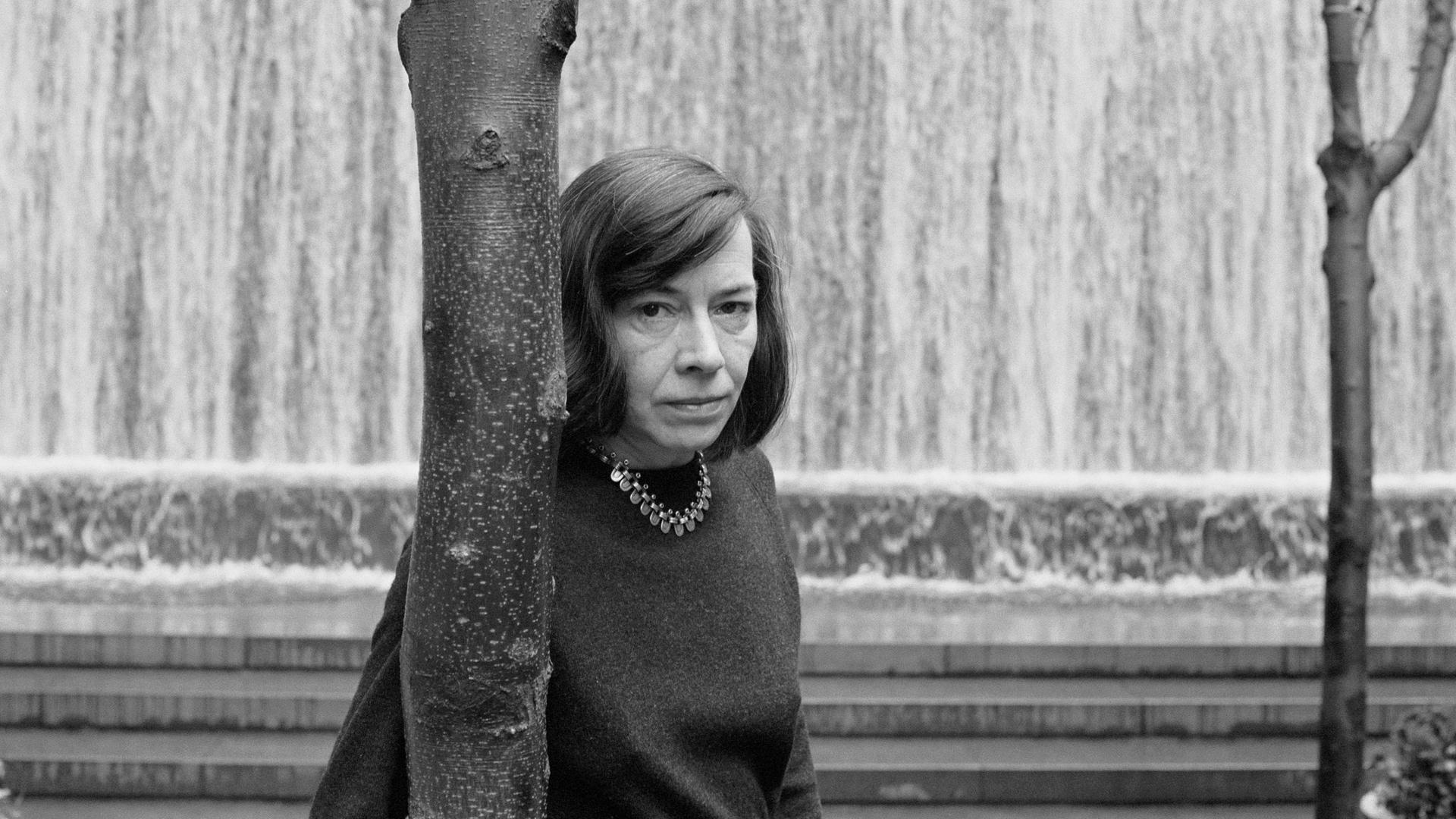 Patricia Highsmith lehnt sich an einen Baum und schaut dem Fotografen intensiv entgegen.