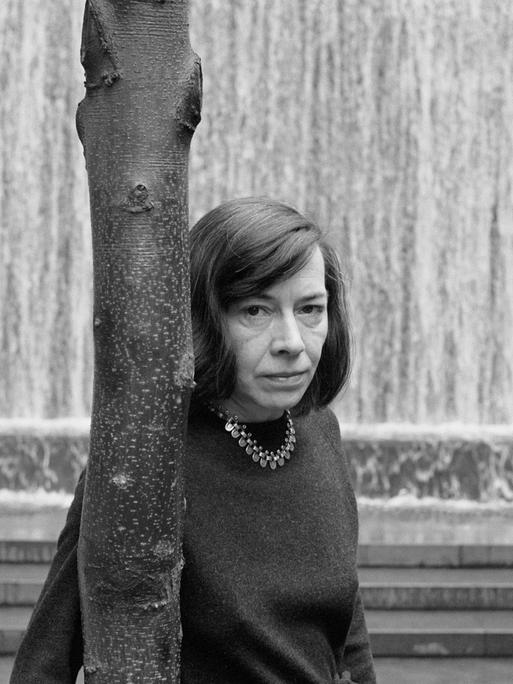 Patricia Highsmith lehnt sich an einen Baum und schaut dem Fotografen intensiv entgegen.