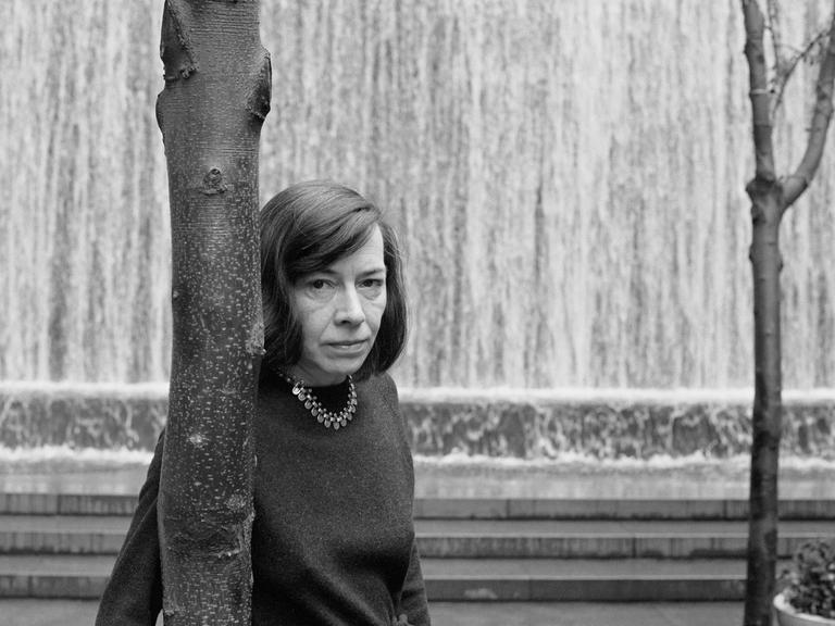 Patricia Highsmith lehnt sich an einen Baum und schaut dem Fotografen intensiv entgegen.