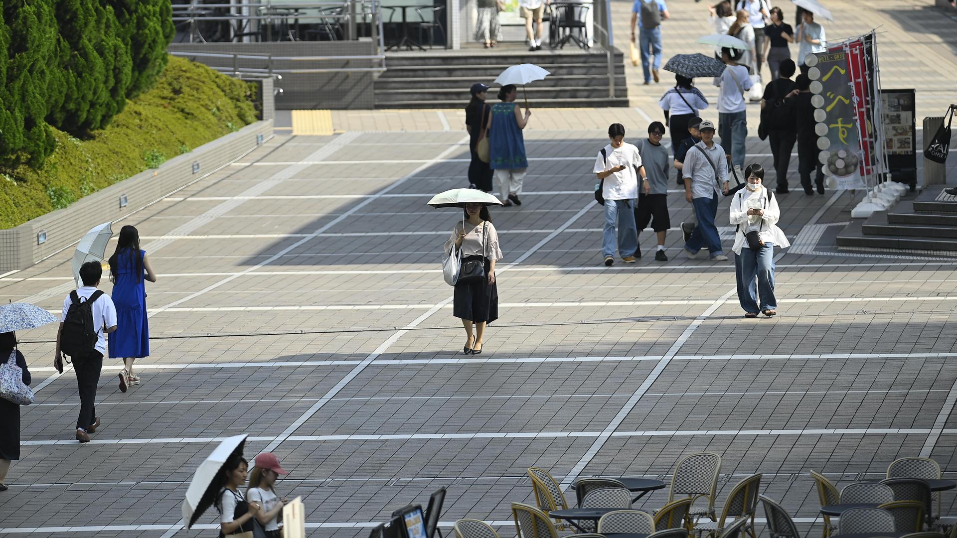 Menschen gehen bei großer Hitze mit Regenschirmen zum Schutz auf einer Straße in Tokio.