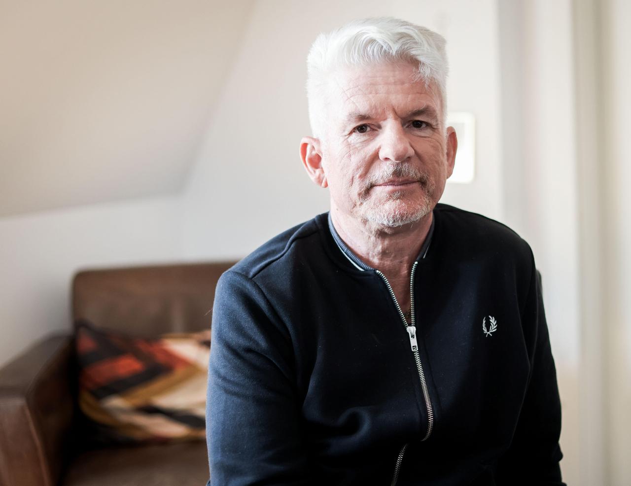 Heinz Strunk blickt in einer lichten Wohnung ernst in die Kamera