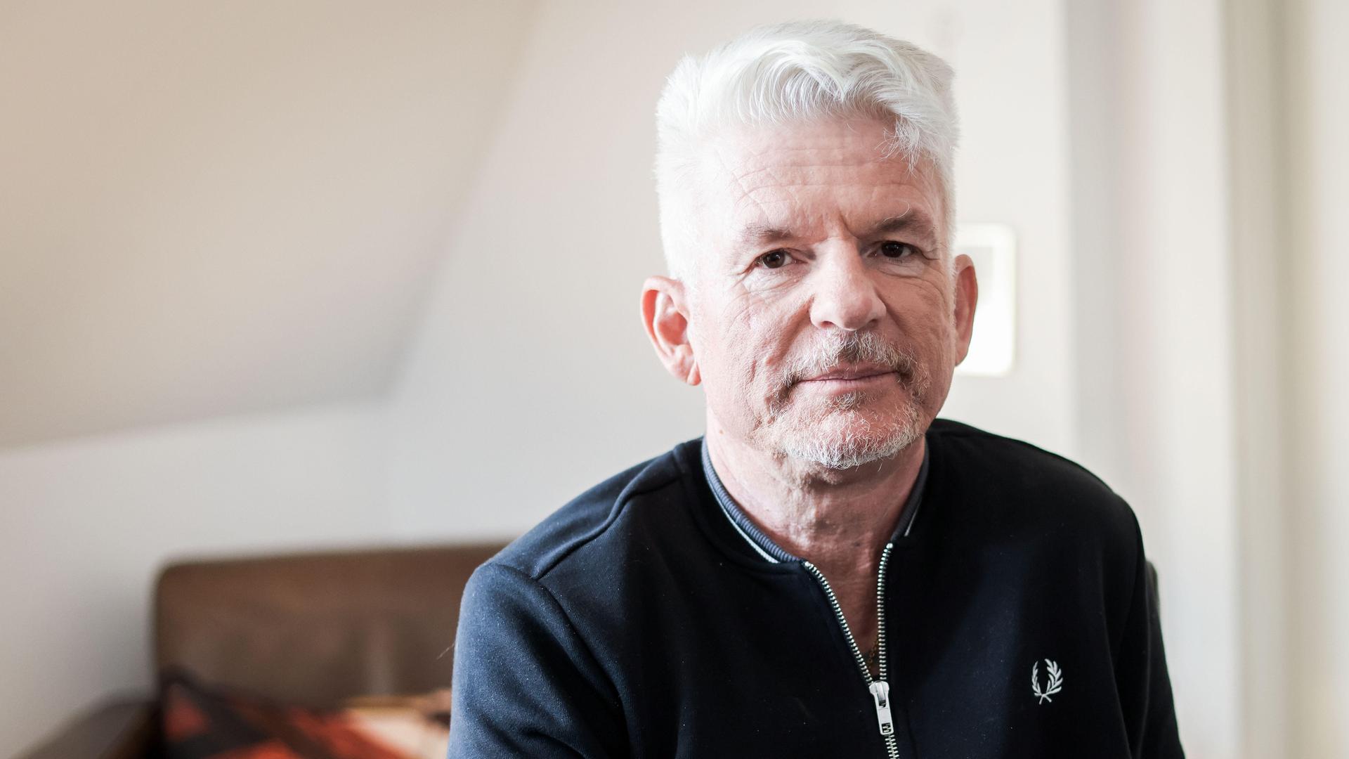 Heinz Strunk blickt in einer lichten Wohnung ernst in die Kamera